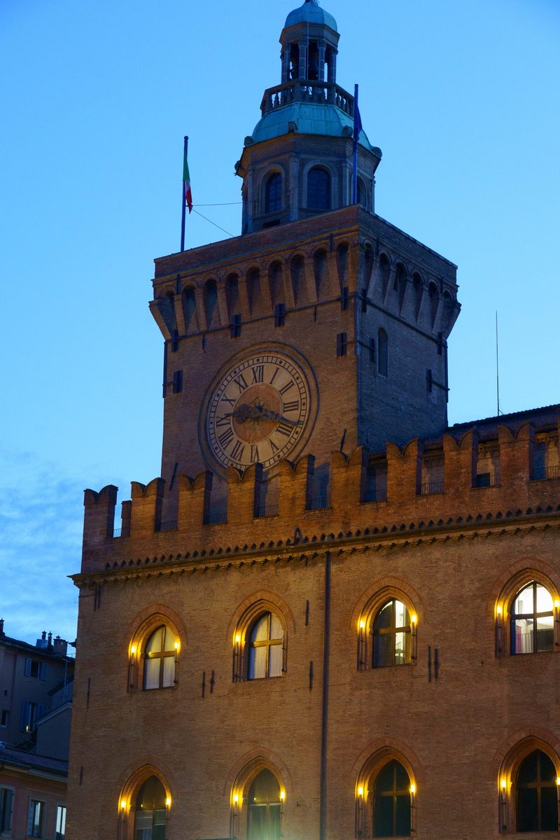 The illuminated clock tower of Palazzo d'Accursio at dusk in Bologna