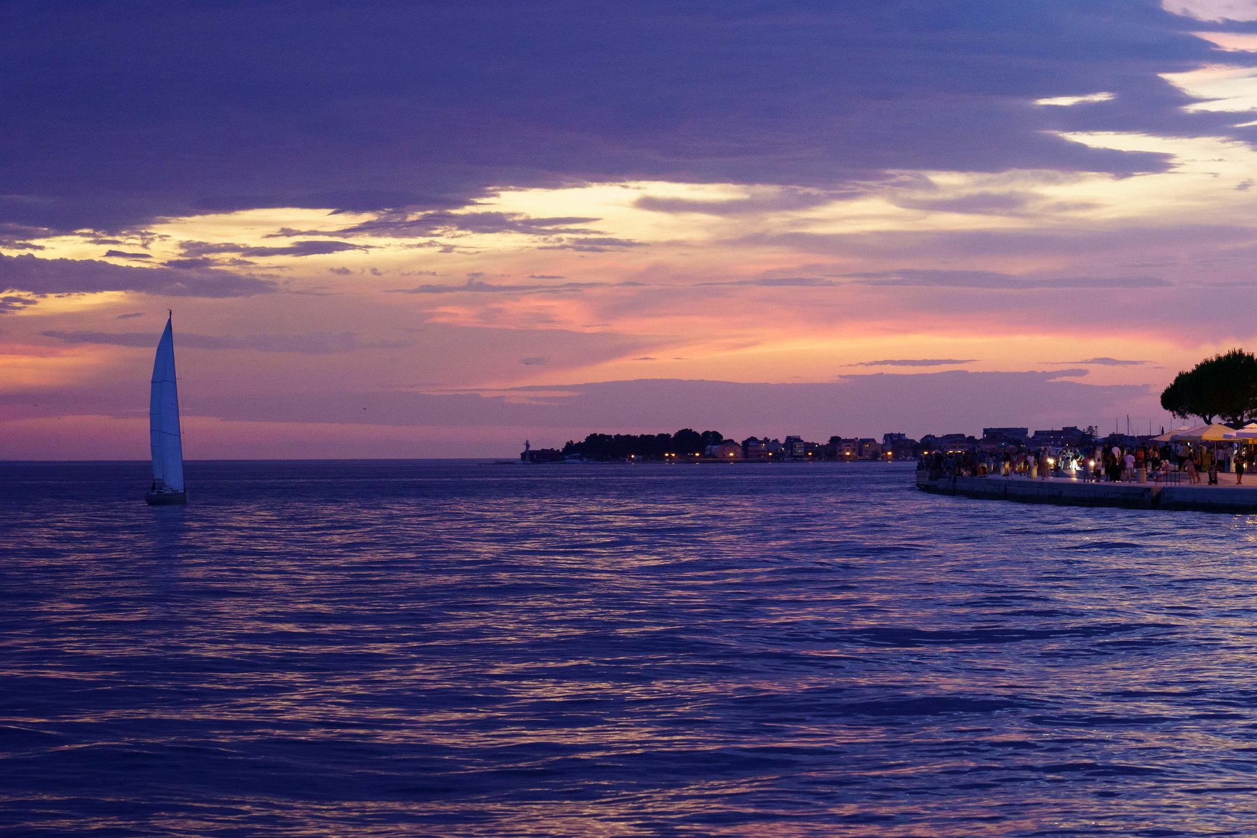 Sailboat gliding past the promenade under a pink and purple twilight sky