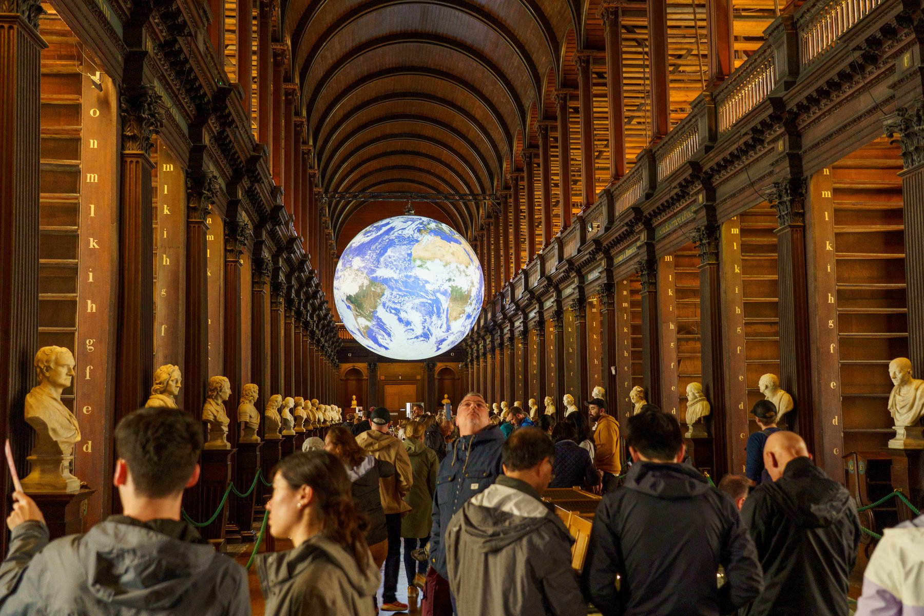 Visitors beneath a large illuminated globe suspended in the Long Room at Trinity College