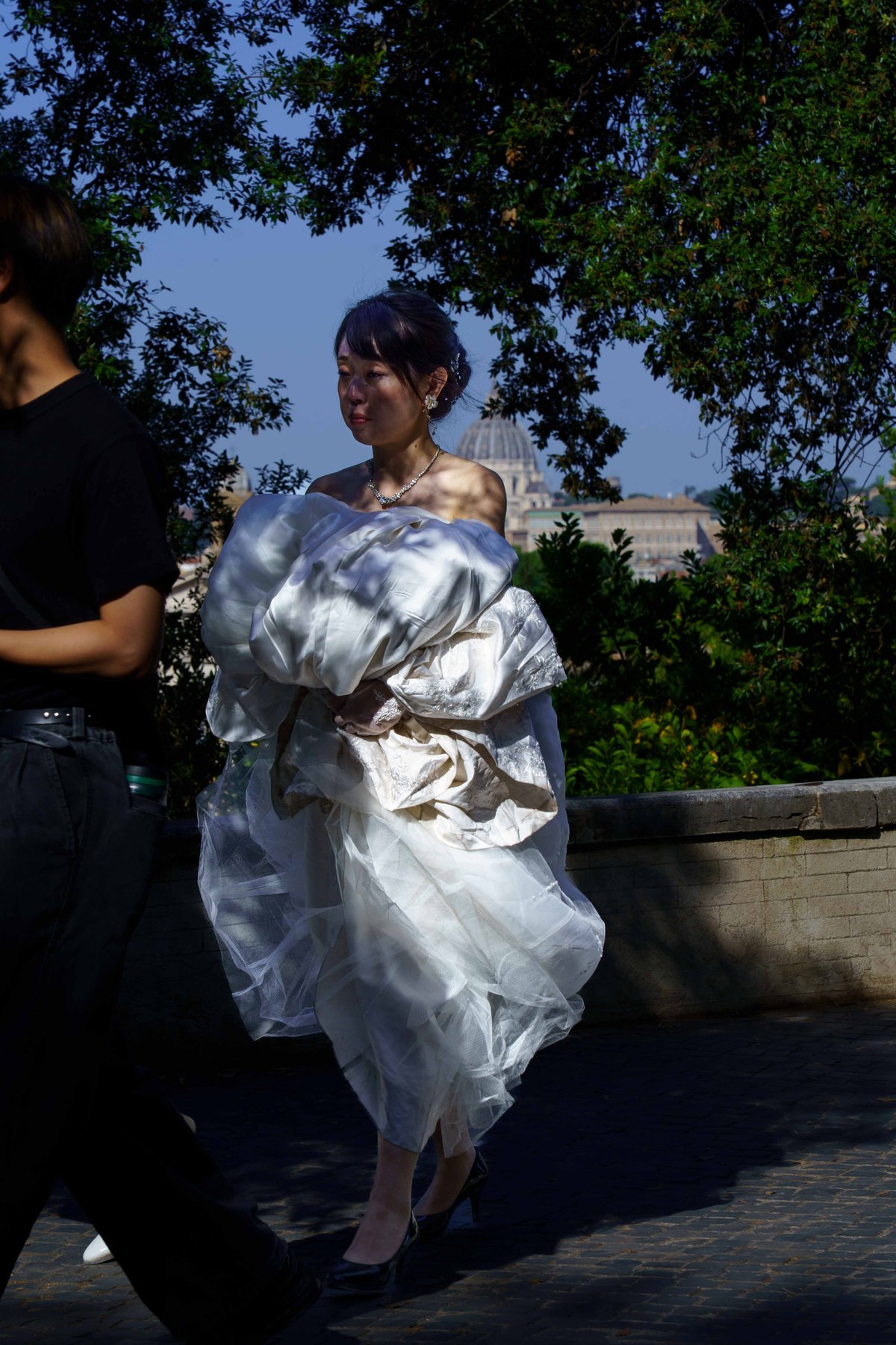 A woman in a wedding dress crossing a terrace with St. Peter's Basilica in the distance