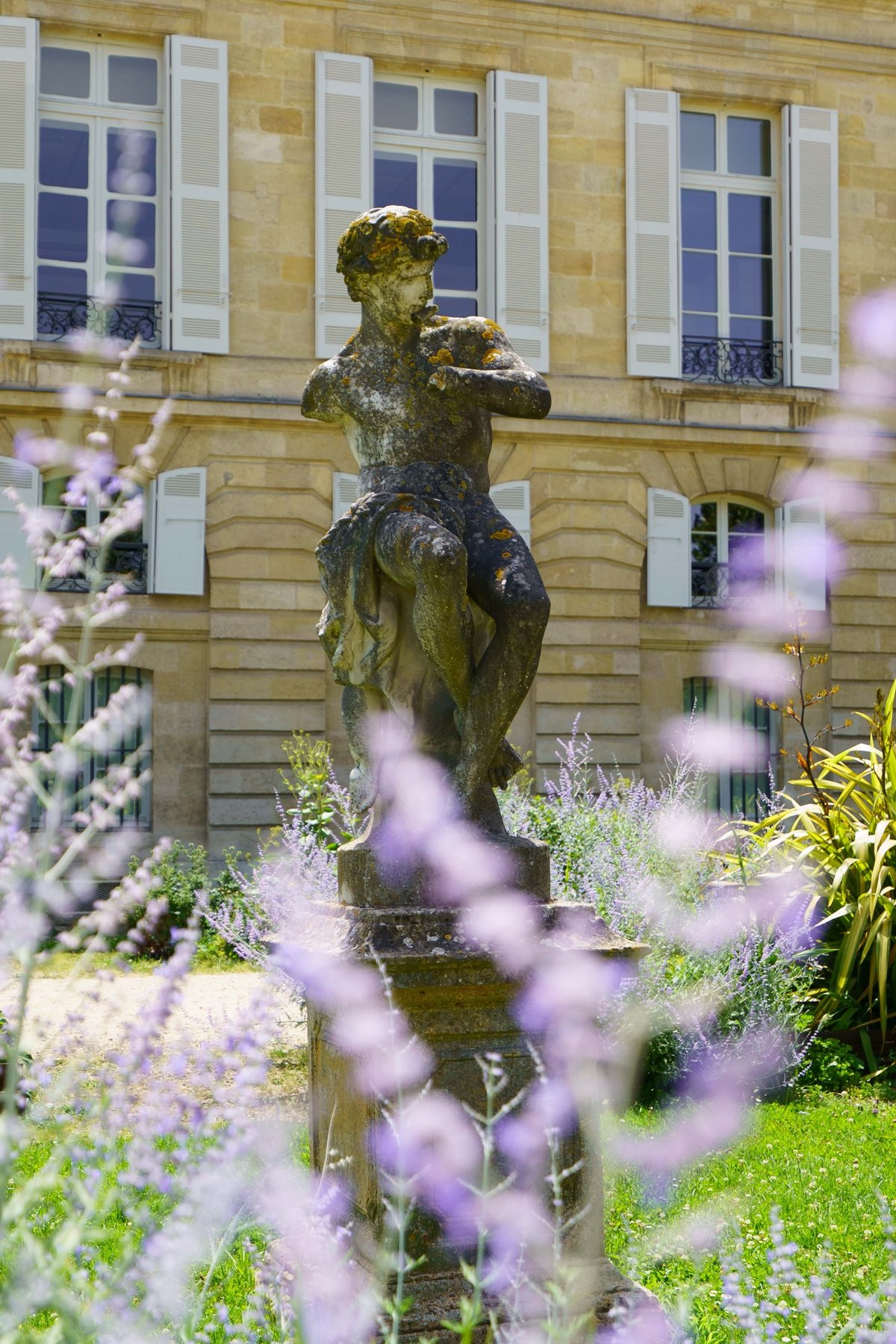 A weathered statue in the back of the Jardin Public in Bordeaux, Russian sage blooming around it