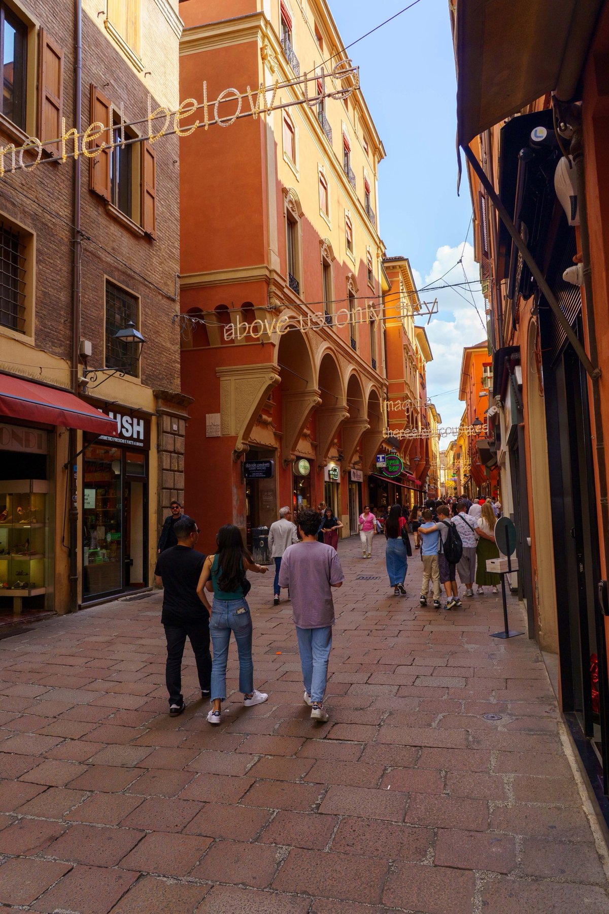 A porticoed street in Bologna strung with a neon art installation quoting the song Imagine