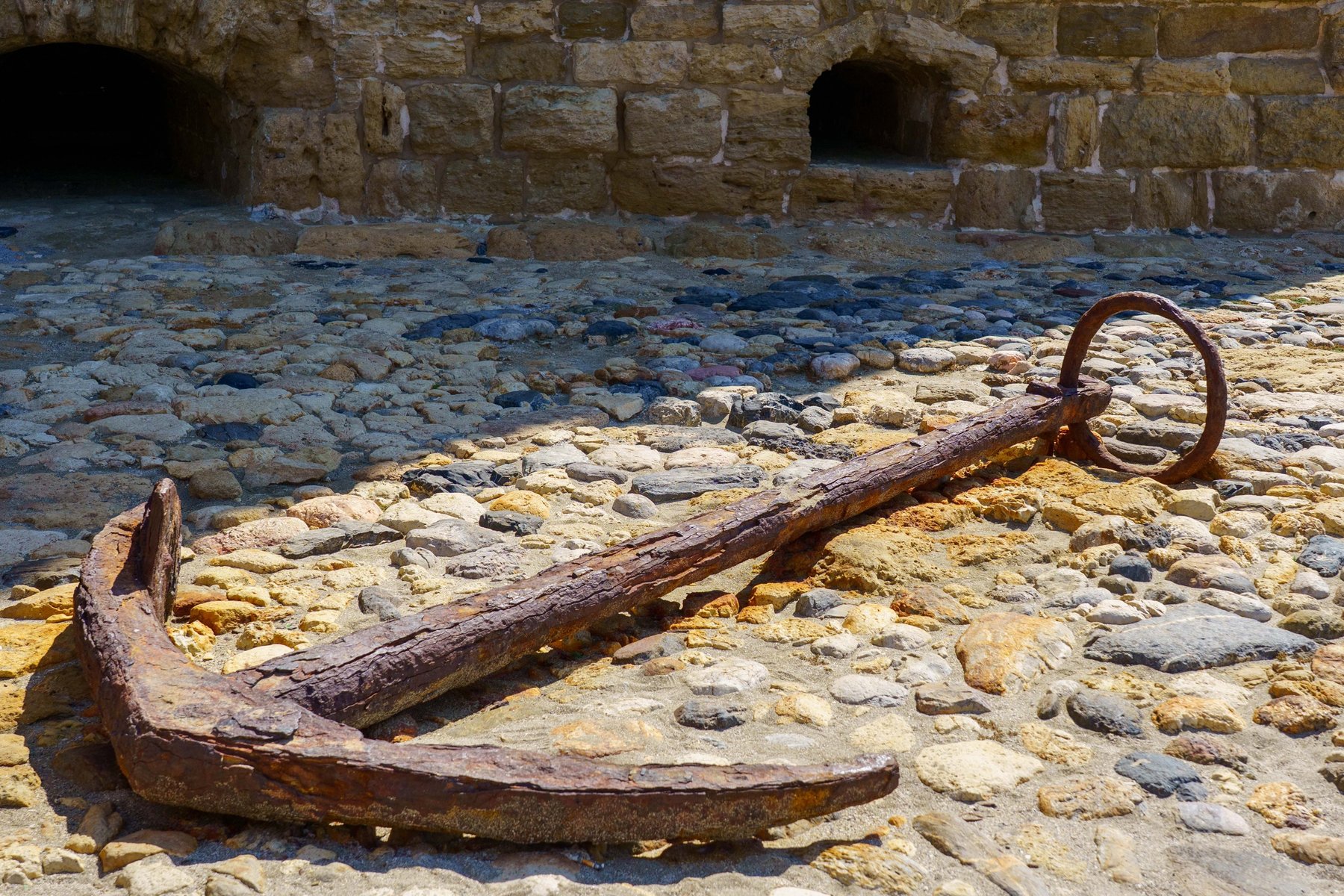 An old iron anchor resting on the cobblestones inside Koules Fortress