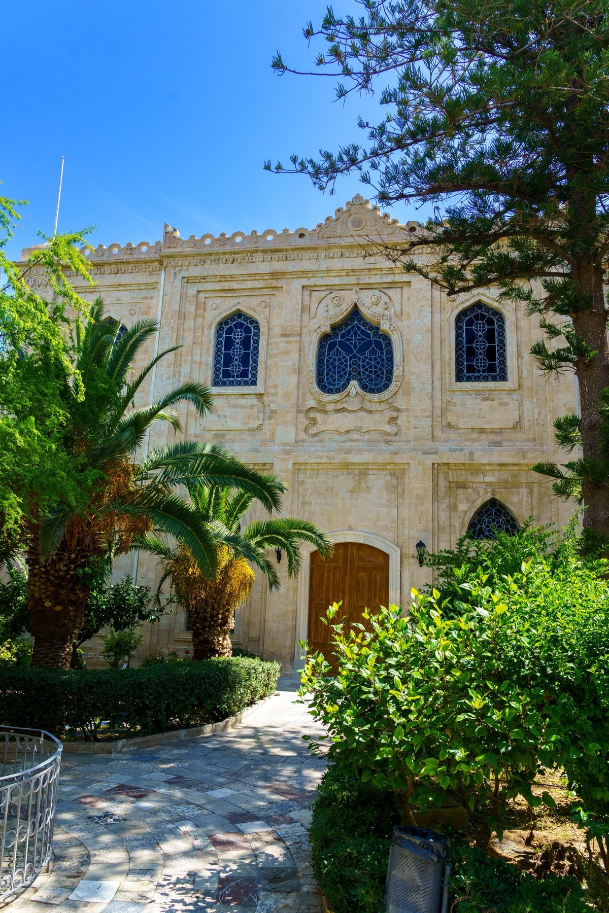 An ornate stone building with Moorish-arched windows framed by palms in Heraklion