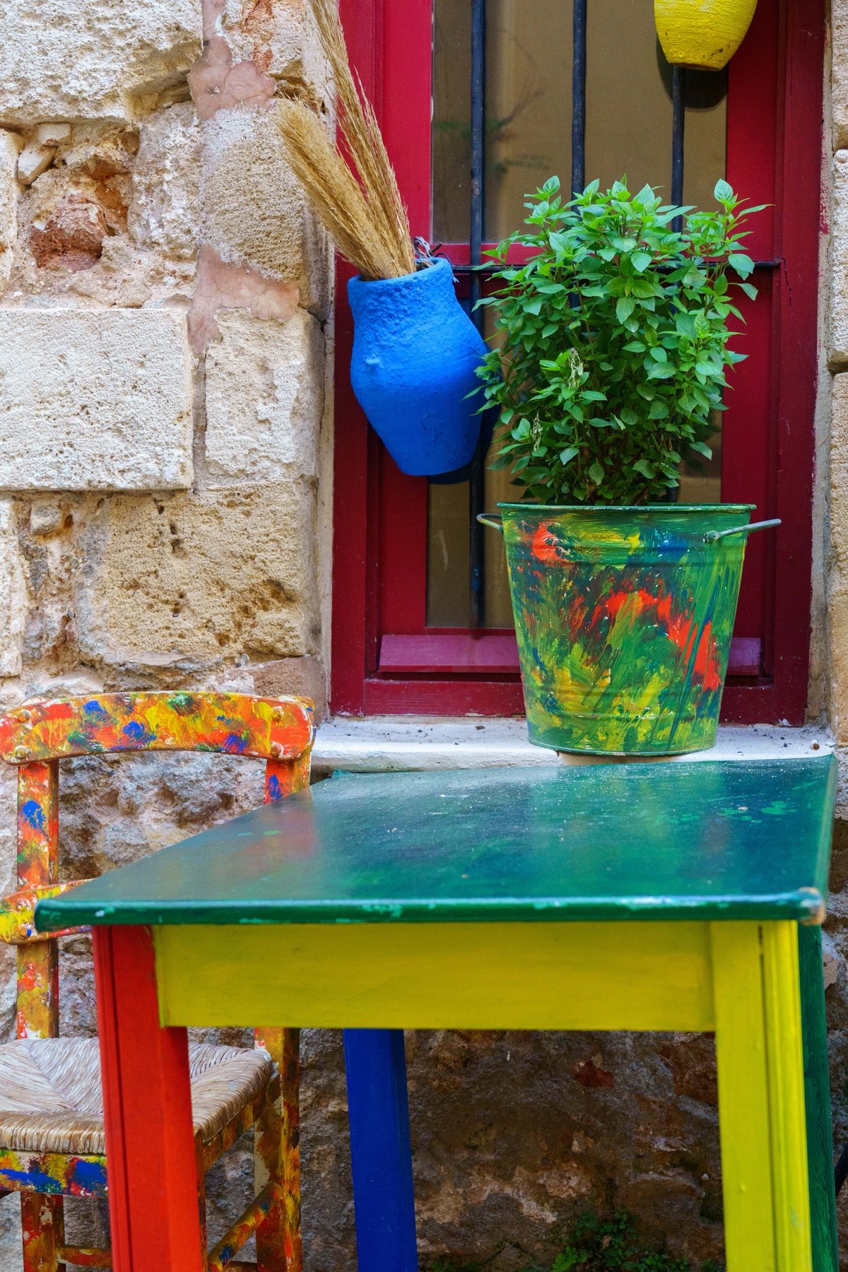 Hand-painted furniture and pots outside a red doorway in Crete