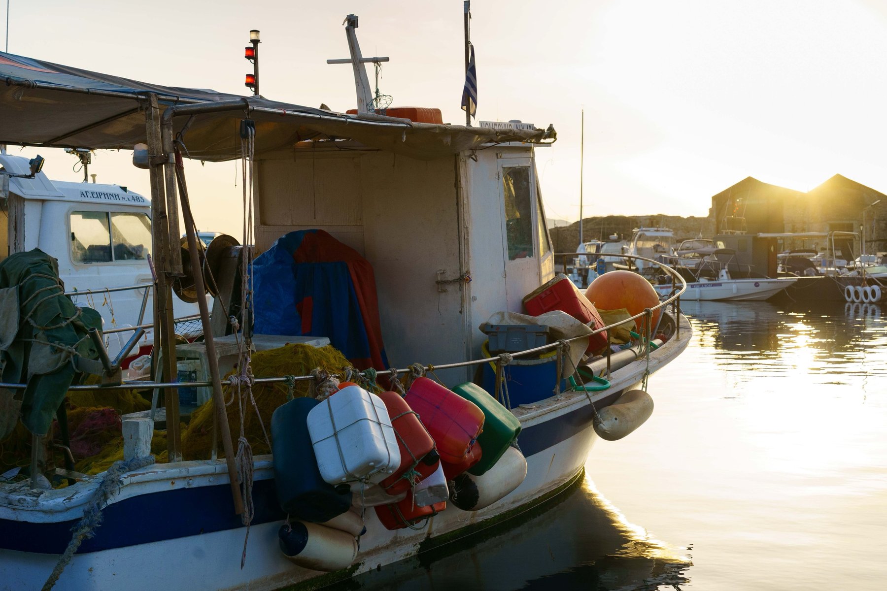 A fishing boat rigged with buoys and gas cans at sunrise in Chania's harbor