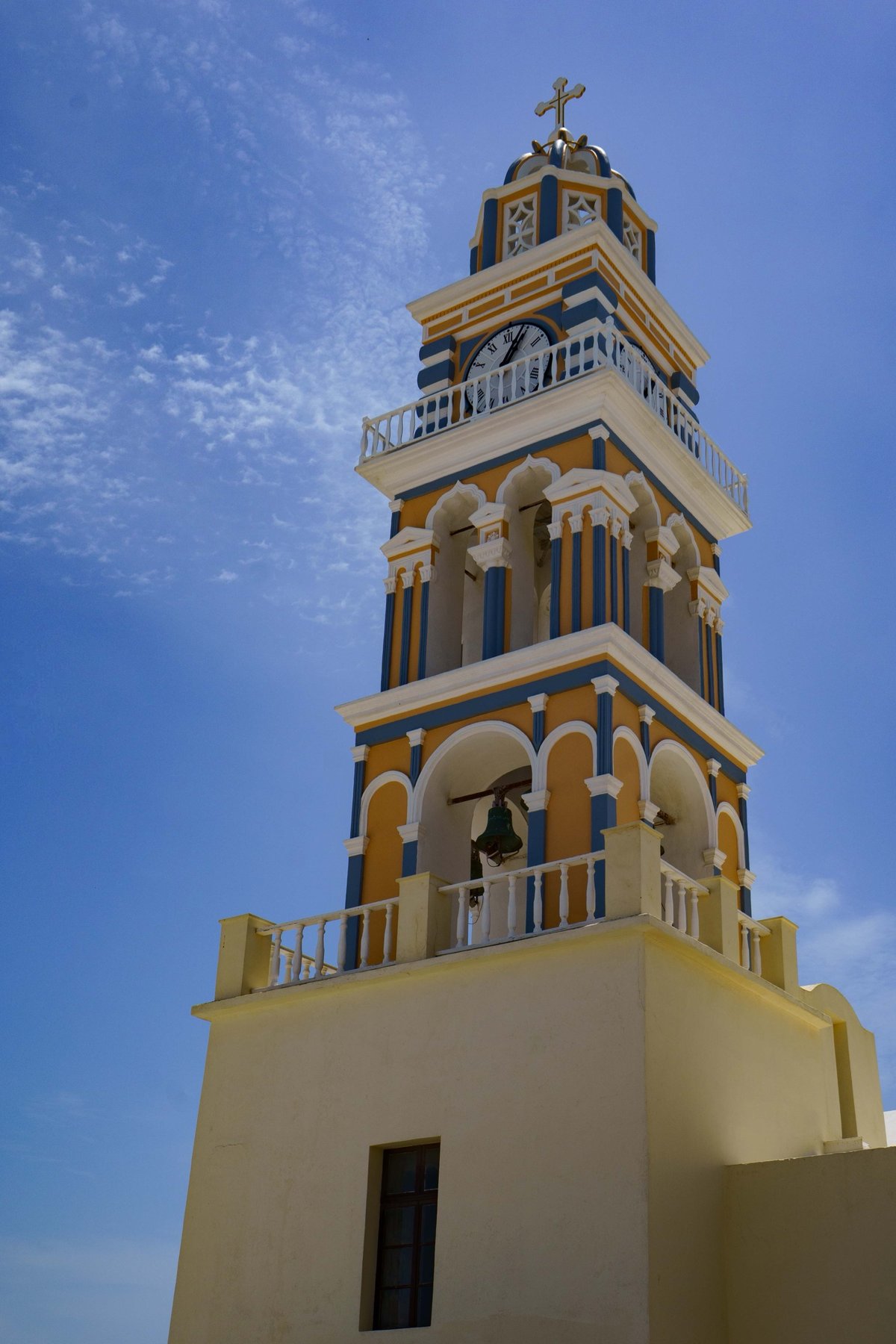 A yellow and blue church bell tower along the Santorini caldera walk