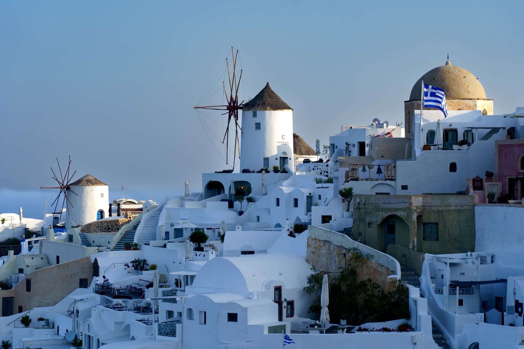 Oia's windmills at dusk with a Greek flag flying above the domes
