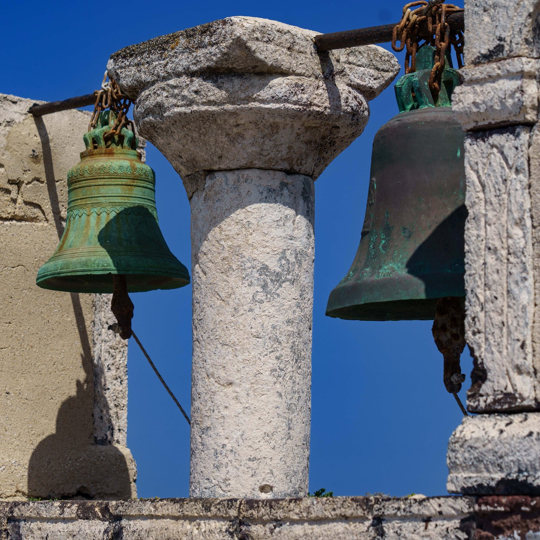 A close-up of weathered bronze bells on an Oia bell tower in Santorini