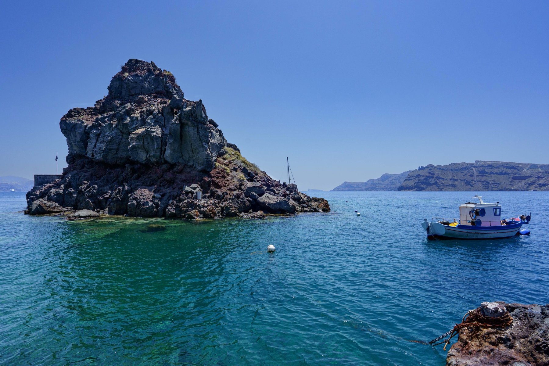 A volcanic rock rising from the water at Ammoudi Bay with a fishing boat moored alongside
