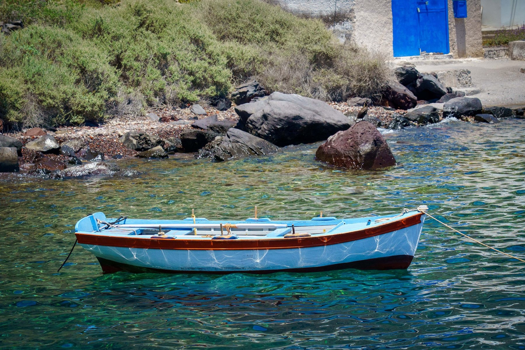 A small fishing boat moored by a blue door along Oia's shoreline in Santorini