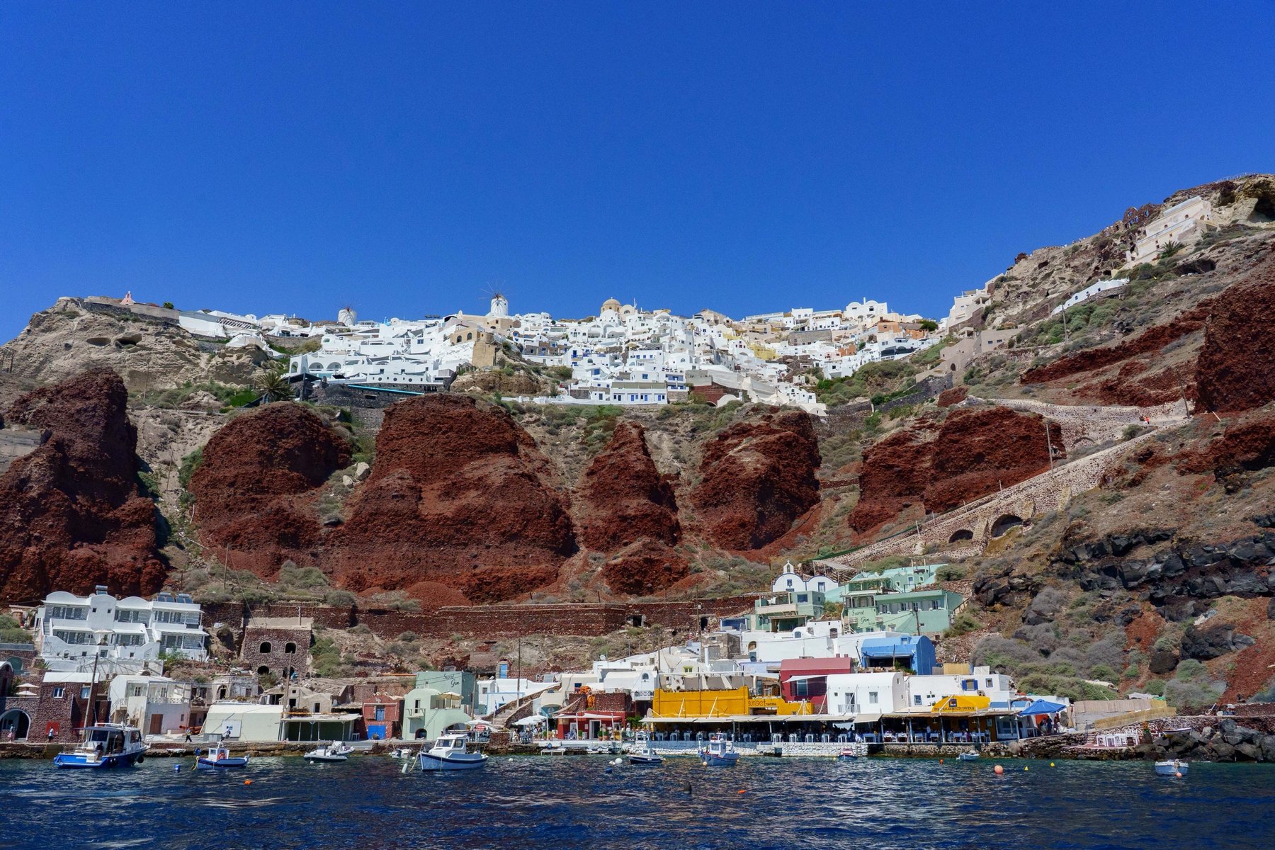 Ammoudi Bay's harbor and red volcanic cliffs seen from the water in Santorini