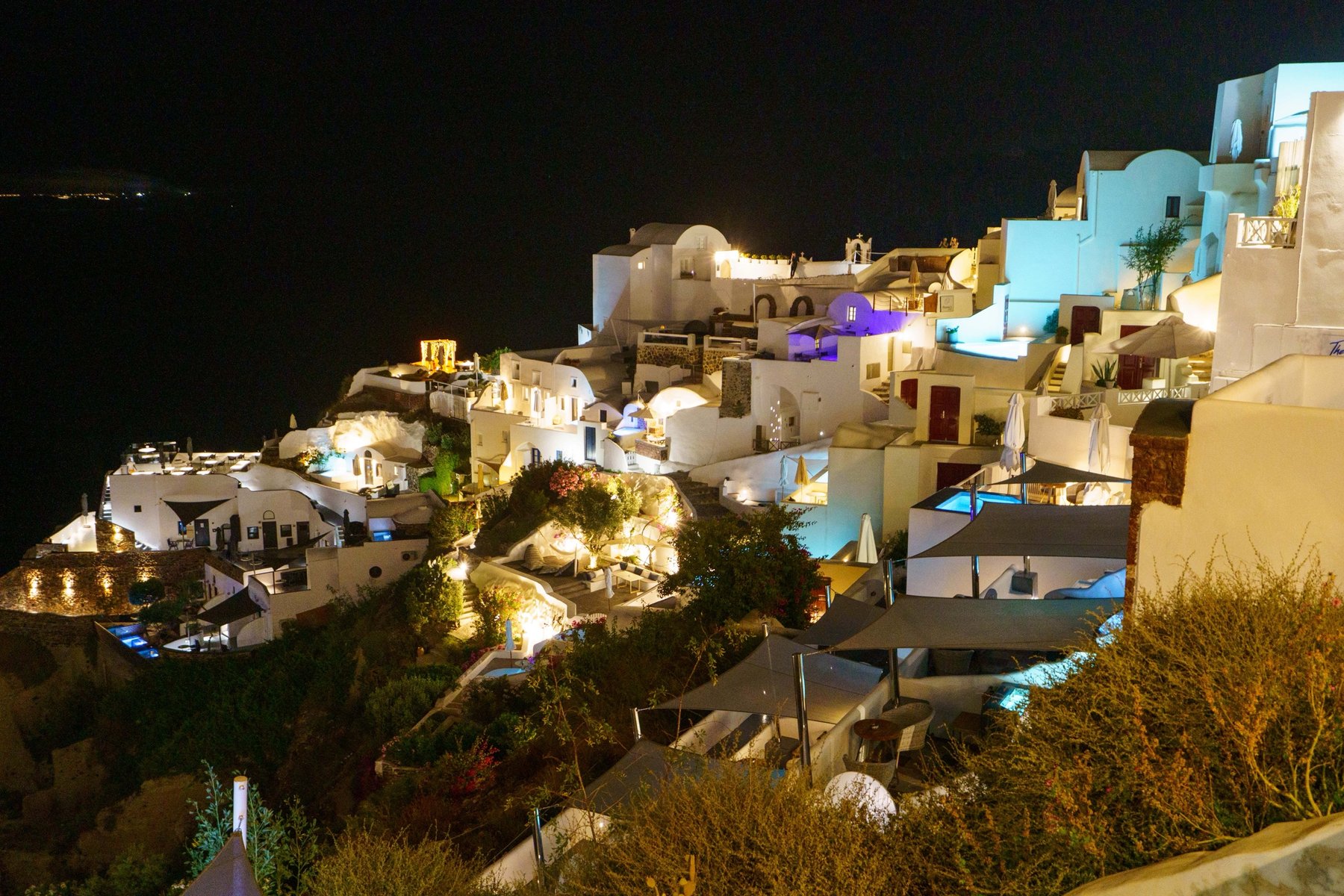 Oia's cliffside hotels lit up at night in Santorini