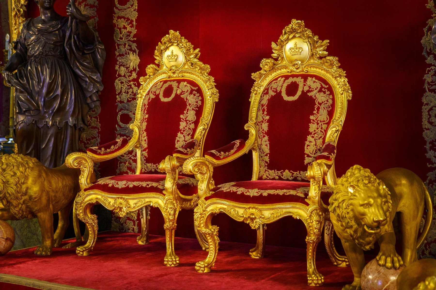 A pair of gilded red velvet throne chairs flanked by bronze lion statues
