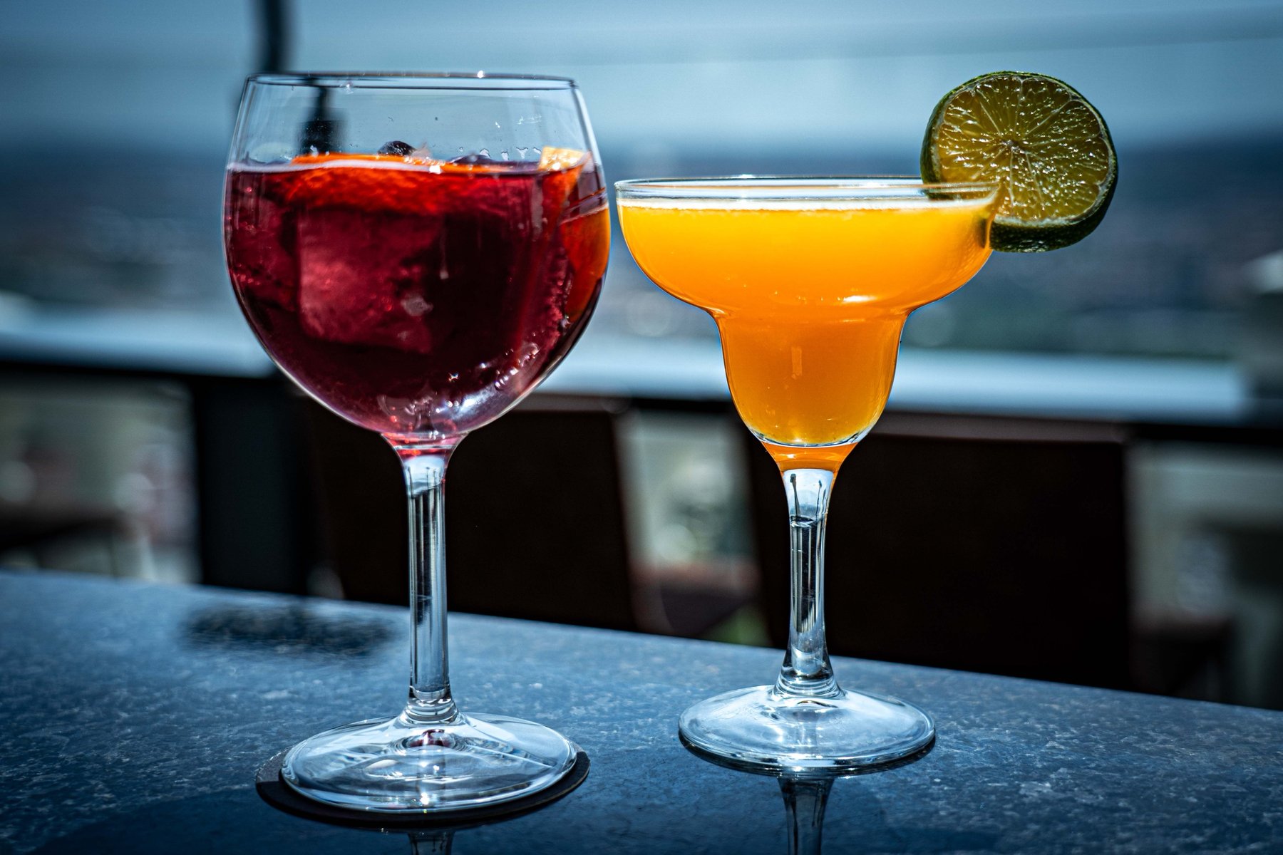 A glass of sangria and a passionfruit margarita on a rooftop bar table