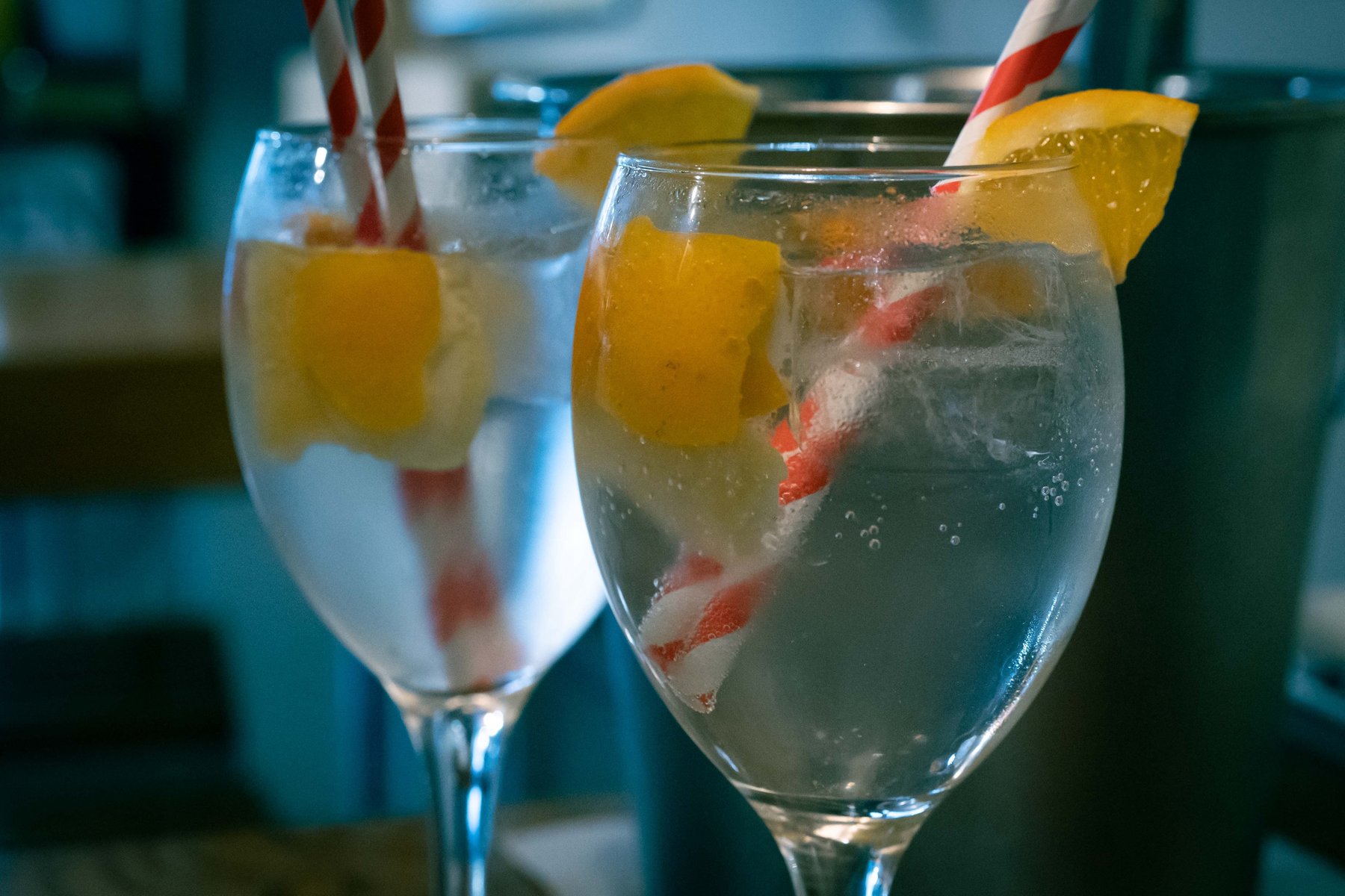 Two gin tonics garnished with orange and lemon in wine glasses