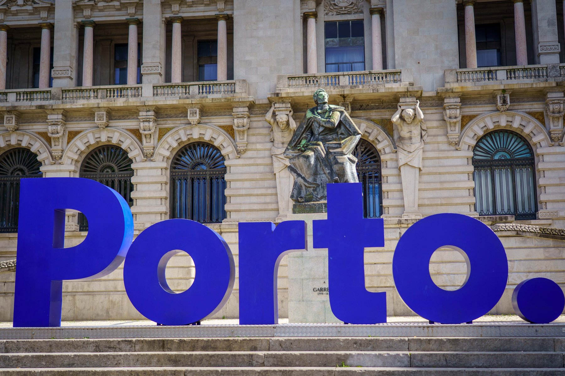 Large blue letters spelling Porto in front of the Almeida Garrett statue