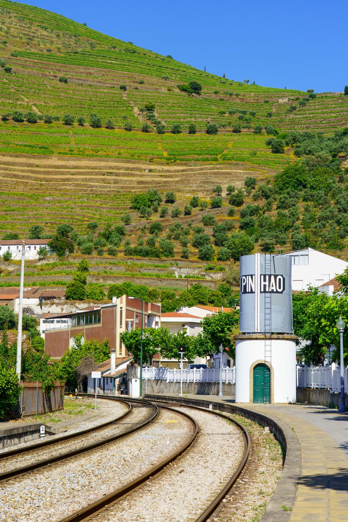 The Pinhão train platform with a water tower stenciled Pinhao and terraced vineyard hillsides above
