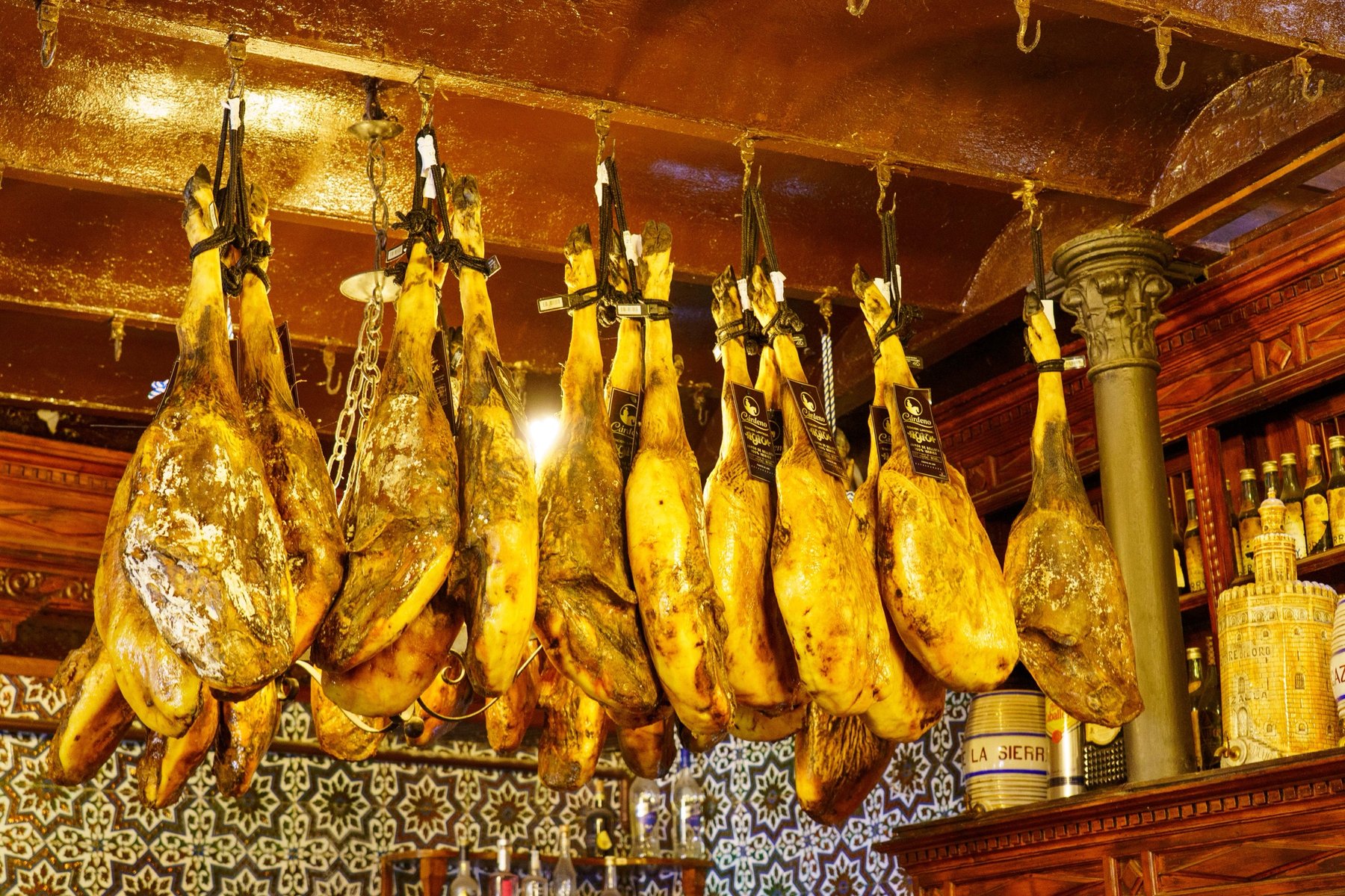 Jamón legs hanging from hooks above a tiled bar at El Rinconcillo